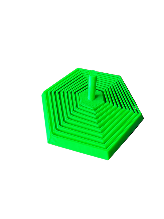 A bright green 3D-printed hexagonal nesting toy or puzzle with concentric square patterns and a central post, resting on a wooden tabletop.